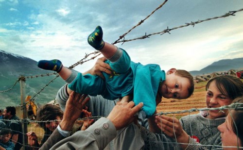 Dvouletý uprchlík z Kosova Agim Shala je předán přes ostnatý plot do rukou prarodičů v táboře uprchlíků v Kukes v Albánii